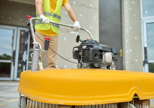 Workman applying a road sweeper on the construction site Cropped photo of a worker cleaning the outdoor floor tiles with a street sweeping machine